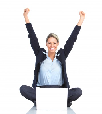 Extraordinary Woman sitting on the ground in front of her laptop with her arms up in celebration while she smiles at the camera