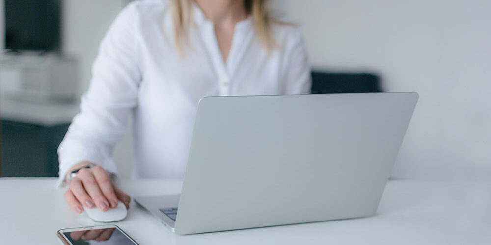 Recruitment-Best-Practices woman at a laptop with her phone on the desk