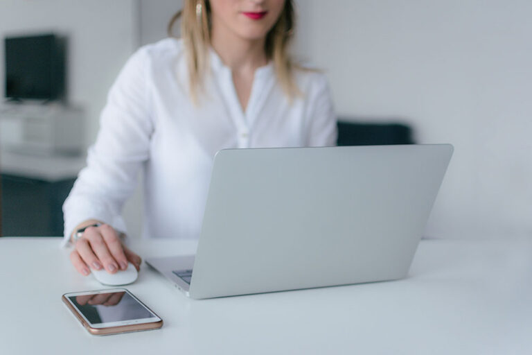 Recruitment-Best-Practices woman at a laptop with her phone on the desk
