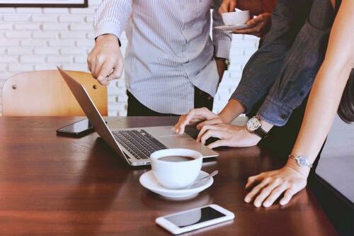 With the prevalence of an online presence, companies are on the hunt for qualified UX designers. group of employees huddled over computer