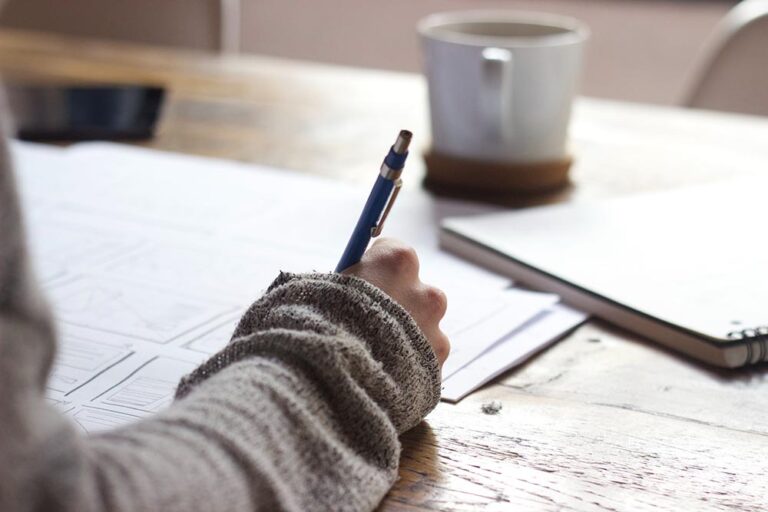 Content Writing vs. SEO Writing vs. Copywriting Jobs: What’s the Difference? coffee on desk with person writing on papers