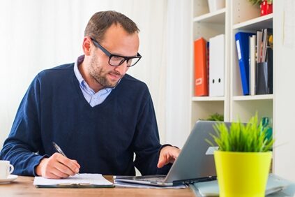 A marketer's job is colorful, to say the least. man writing on a clipboard as he scrolls on his laptop