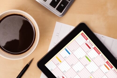 Design your content calendar with these tips in mind. overhead close up of a tablet a computer and a cup of coffee sitting on a desk