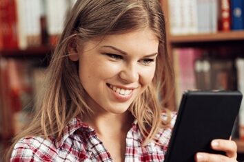 Global ad trends show mobile is taking off Woman smiling in a library scrolling on a tablet