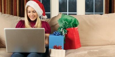 holidayjobsearch woman in a santa hat working on her laptop with gifts beside her