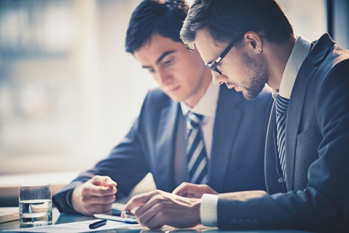In an age when big data and online media platforms dominate marketing strategies, the discussion surrounding the relationship between the chief marketing officer and chief information officer continues to grow. two men looking at a tablet at a table