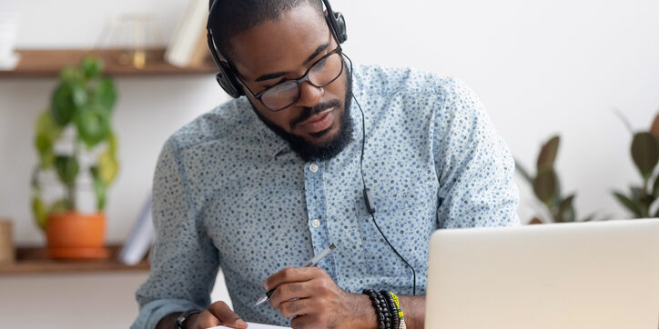 Focused african businessman in headphones writing notes watching webinar man at computer writing on note pad_job search tips