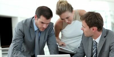 partnership 3 coworkers crowd around a computer to look at something