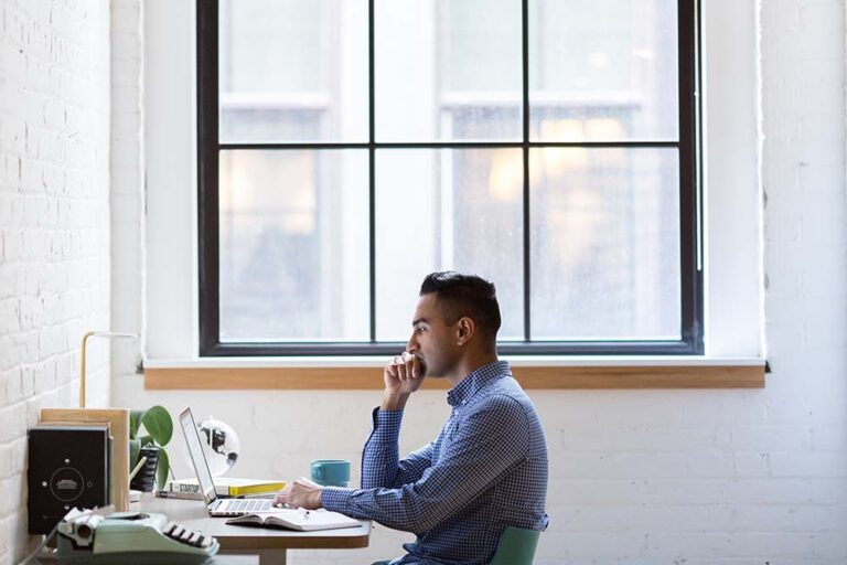 recruiter-guy-recruiting-UX-designers man working at his desk on a laptop in front of a window