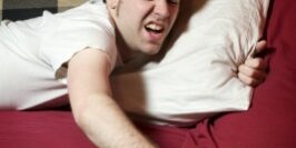 uncomfy man hitting snooze on his alarm