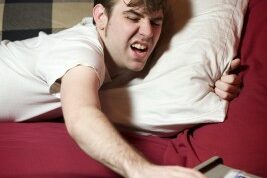 uncomfy man hitting snooze on his alarm