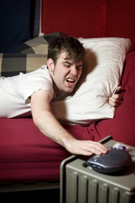 uncomfy man hitting snooze on his alarm