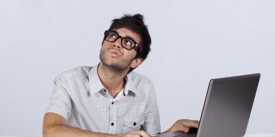 webdev man with a pondering face as he working his laptop looking up