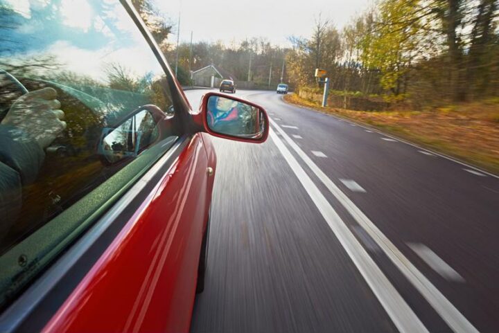 side of a red car driving down a road in the fall