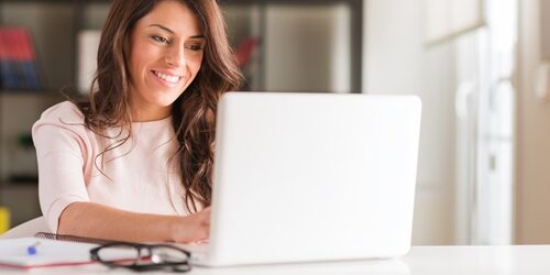 You may not realize it, but the way you communicate in emails is much more important than you think. Woman smiling as she works on her laptop in a bright office