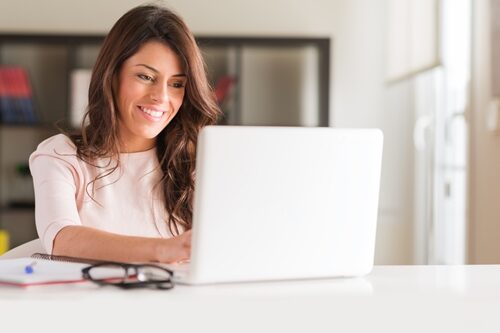 You may not realize it, but the way you communicate in emails is much more important than you think. woman smiling at her laptop as she works in a bright office