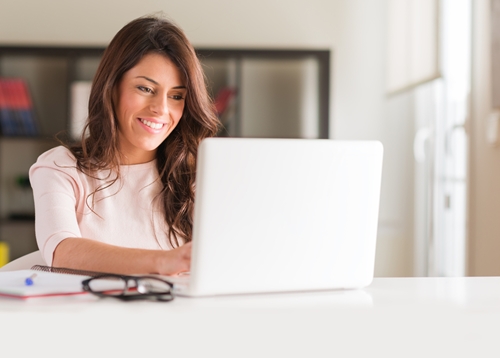 You may not realize it, but the way you communicate in emails is much more important than you think. woman smiling at her laptop as she works in a bright office