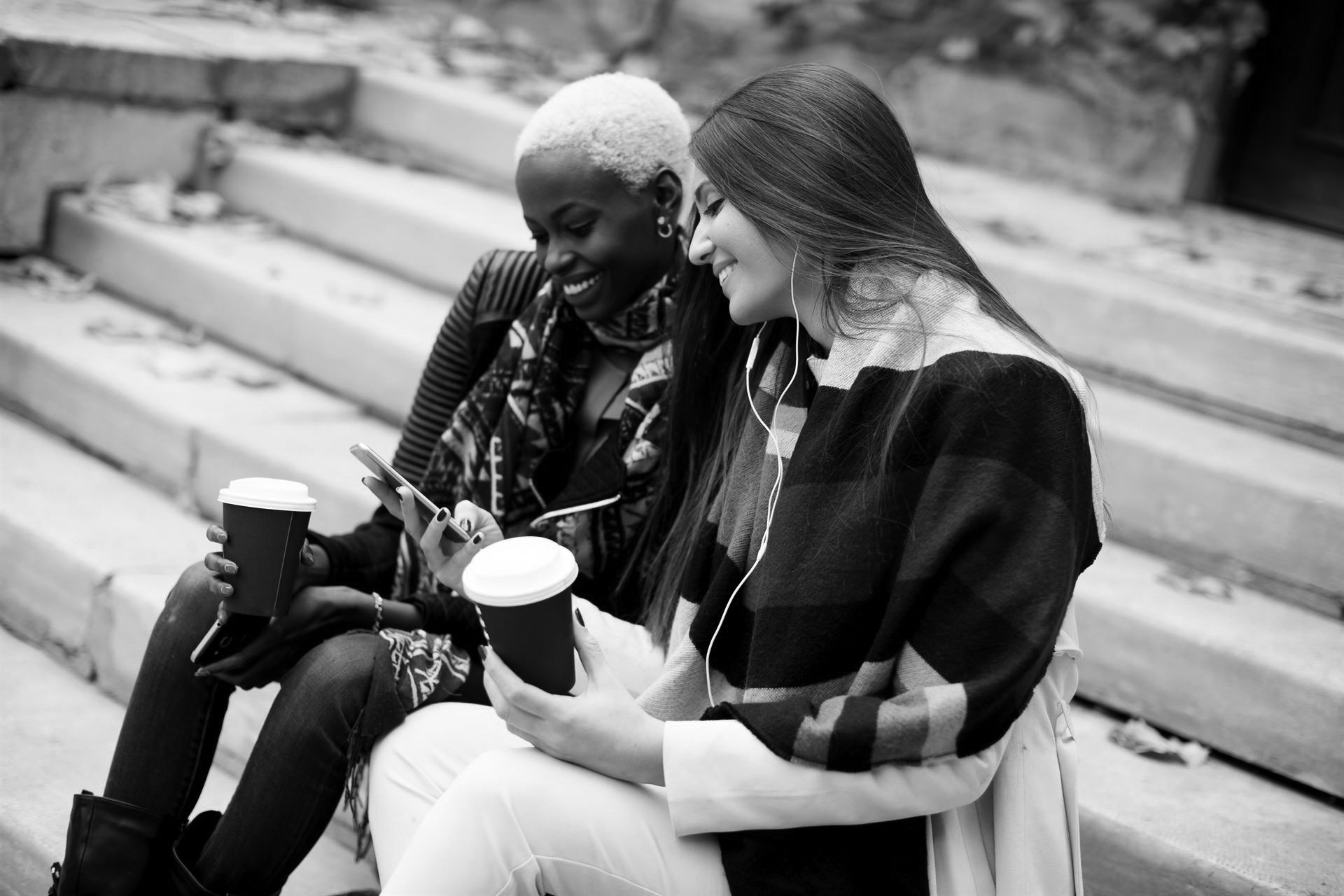 Young friends sitting in autumn park, talking and carry coffee to go in the hands Young friends sitting in autumn park, talking and carry coffee to go in the hands